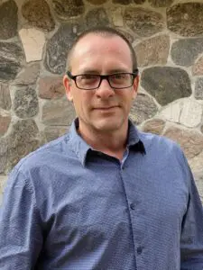 Man in blue shirt, smiling, glasses.