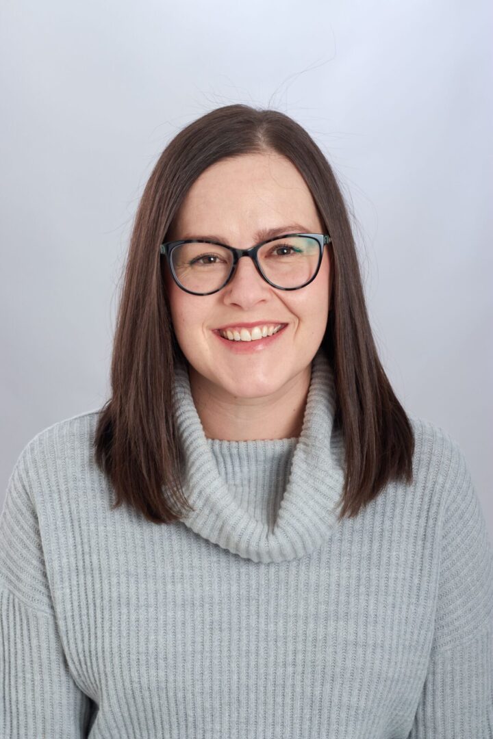 Smiling woman wearing glasses and sweater.