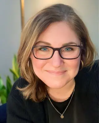 Woman with glasses smiling in portrait.