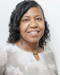 Woman with curly hair smiling in a white shirt.