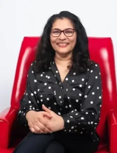 Woman in black polka dot shirt sitting in red chair.