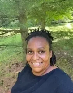 A woman smiles outdoors near a tree.