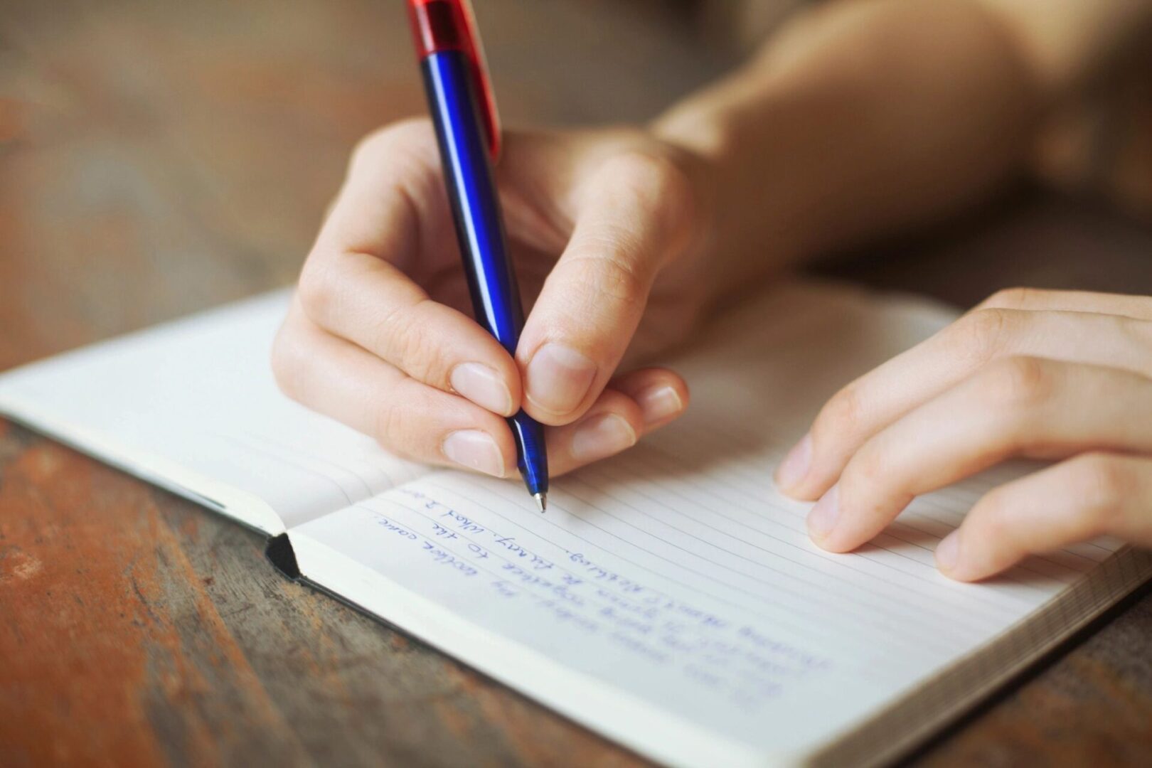 Hand writing in a notebook with a pen.