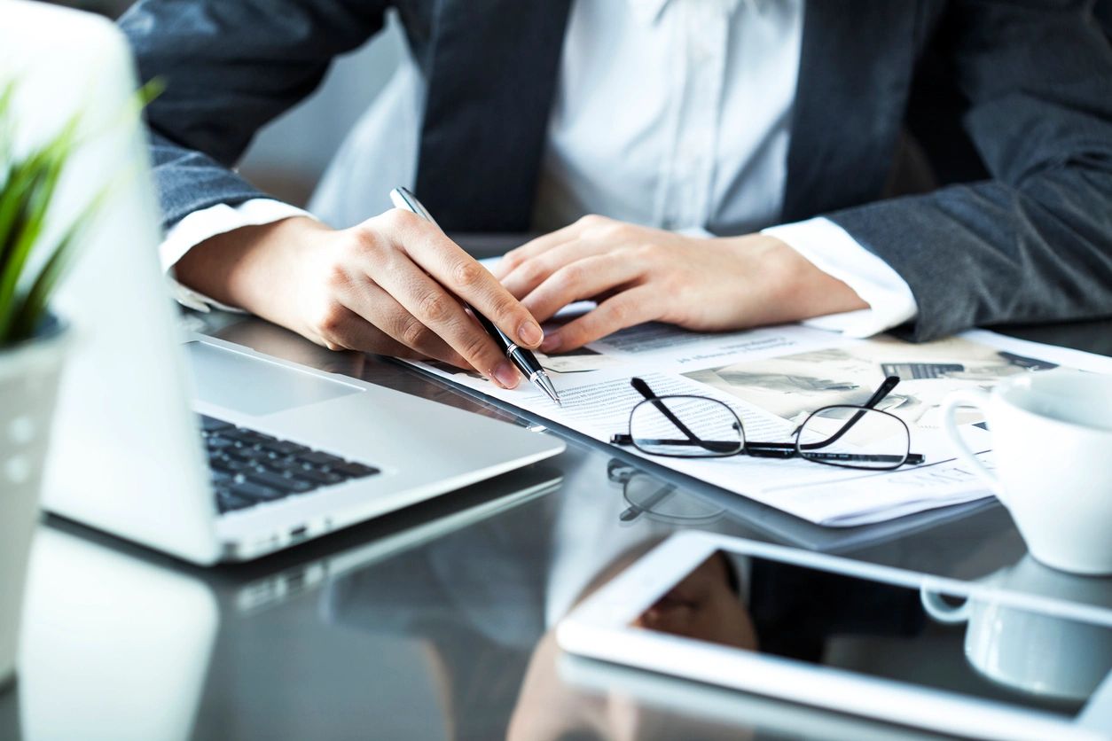 Person reviewing documents with pen and laptop.