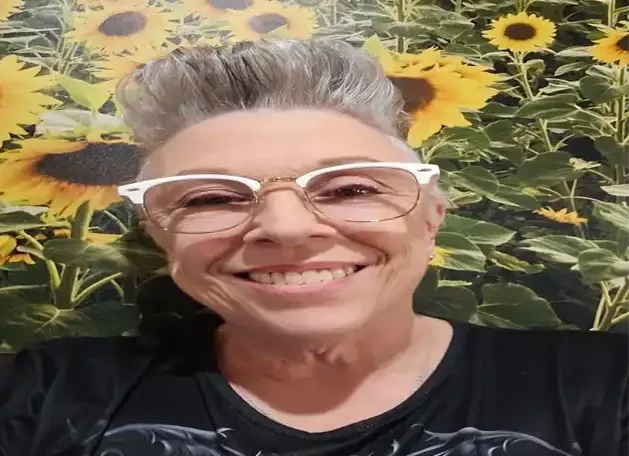 Smiling woman in white glasses with sunflowers behind her.