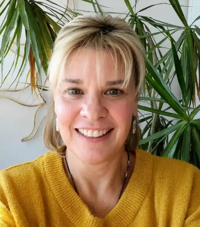 Smiling woman in yellow sweater, plant behind her.