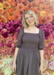 Woman in a grey dress in front of flowers.