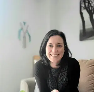 Smiling woman in black sweater on couch.