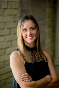 Woman smiling with arms crossed, wearing black top.