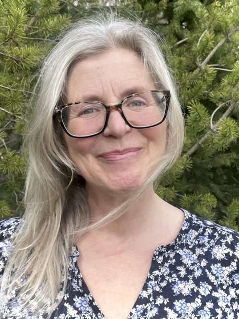 Smiling woman with glasses in nature setting.