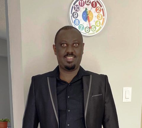 Man in suit standing under colorful wall clock.