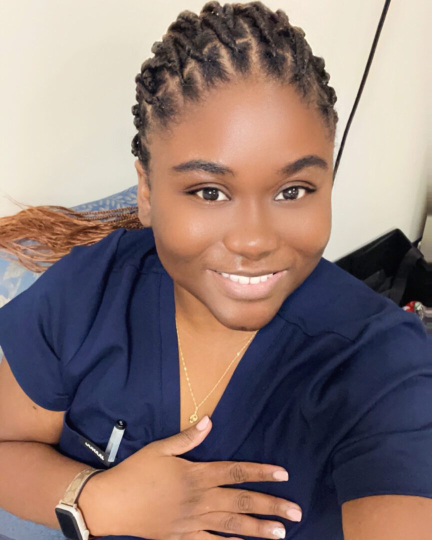 Smiling person in blue scrubs, braided hair.
