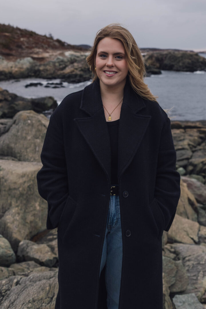 Woman in black coat by rocky shore.