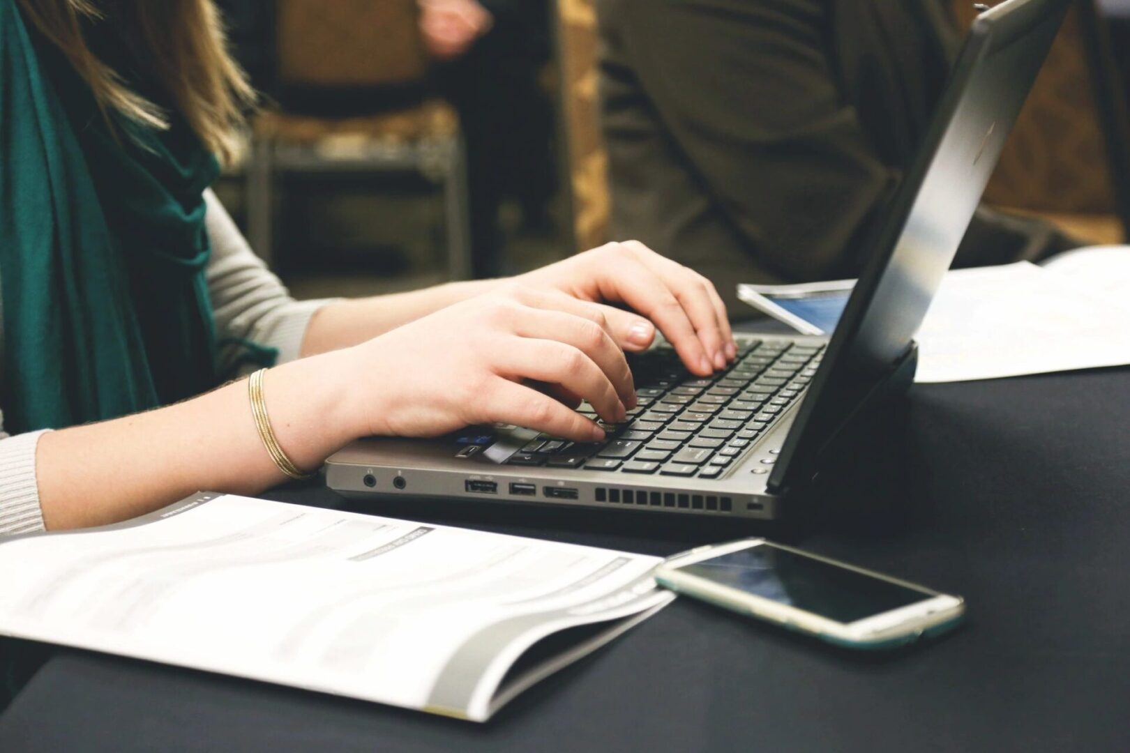 Person typing on laptop with phone nearby.