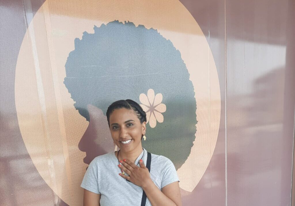 Adonia A woman standing in front of a mural with a flower on it.