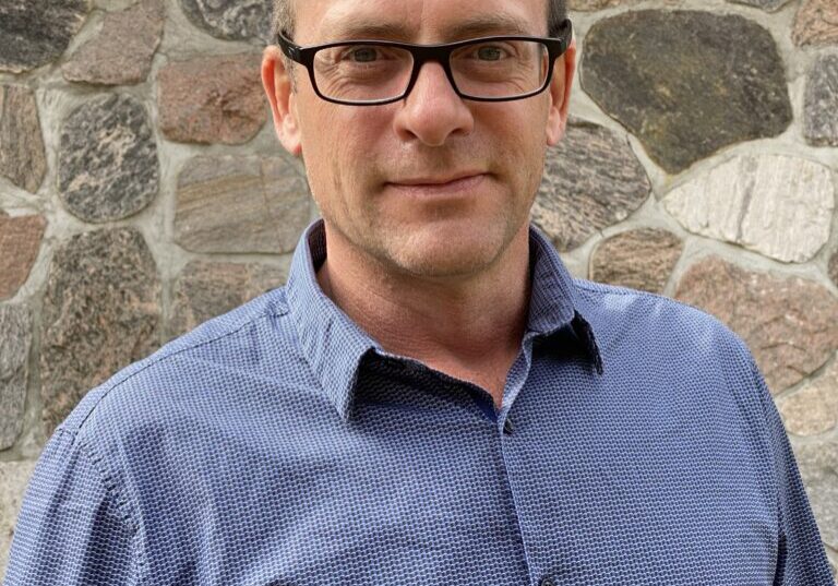Brandon Man in blue shirt, smiling, glasses.