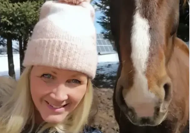 Woman in hat smiling next to horse.