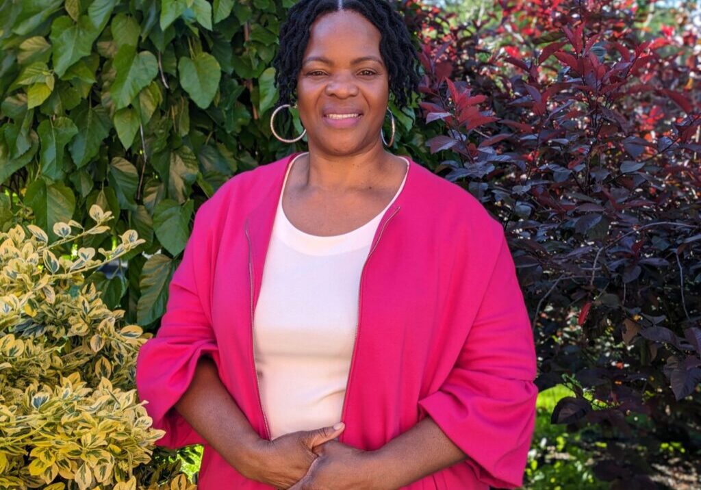 Sandria Bryce 2024 new Woman in pink jacket smiling outdoors.