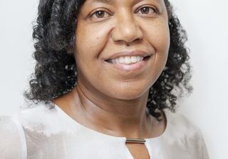 Woman with curly hair smiling in a white shirt.