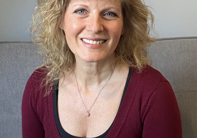 Wendy 3 Smiling woman with curly hair sitting indoors.