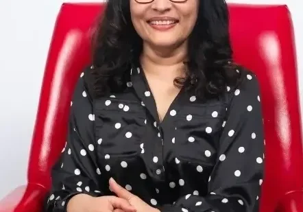 Woman in black polka dot shirt sitting in red chair.