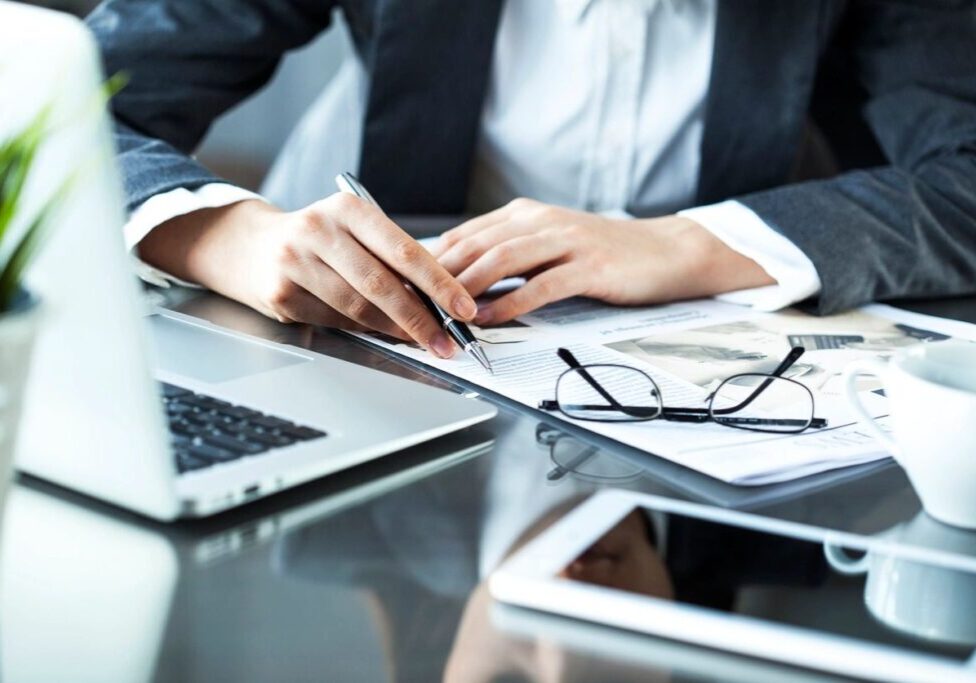 Person reviewing documents with pen and laptop.
