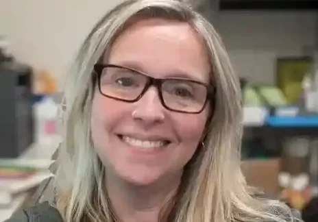 Smiling woman with glasses and necklace.
