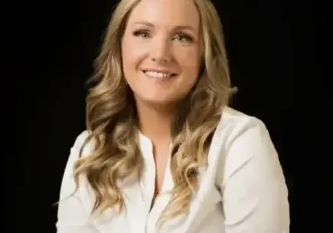 Woman with long blonde hair smiling in white shirt.