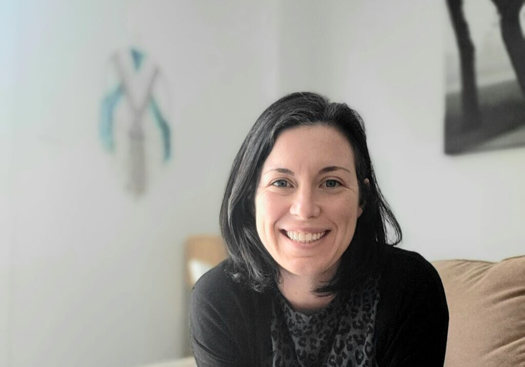 Smiling woman in black sweater on couch.